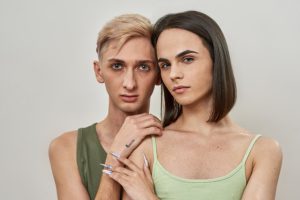 Portrait of couple of two young transgenders looking at camera, posing together isolated over light background. Relationships, lgbtqi, generation Z, love concept